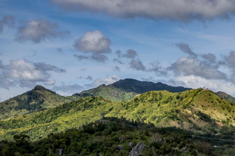 Landscape view of mountains in Rizal covered in trees. Behind them, a blue sky with clouds. 