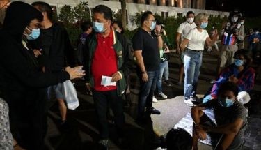 Local officials (L) talk to homeless people, as they distribute face masks to protect themselves from the volcanic ash along a sidewalk in Manila on January 12, 2020, as ash from a volcano in Taal town south of Manila spewed ash into air hand has reached suburban Manila. Philippine authorities warned on January 12, an "explosive eruption" of a volcano south of Manila could be imminent, hours after it sent a massive column of ash skyward that forced officials to halt flights at the capital's main airport until further notice.