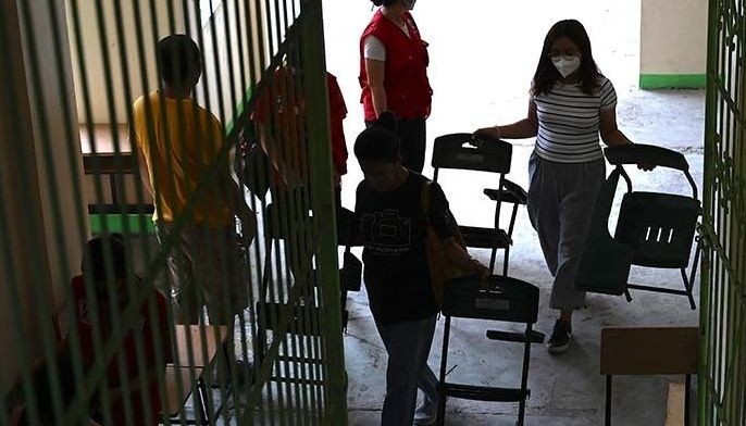 Volunteers carry chairs as they clean classrooms at an elementary school in Manila on August 5, 2022, ahead of the reopening of schools on August 22.