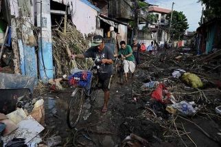 Men carrying their bicycles as they walk along a debris-covered street in Noveleta, Cavite province on October 30, 2022, a day after Tropical Storm Nalgae hit.
