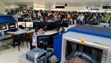 This photo taken on October 4, 2023 shows departing travellers (background) waiting in line for security checks as officials screen carry-on luggage at the Ninoy Aquino International Airport in metro Manila.