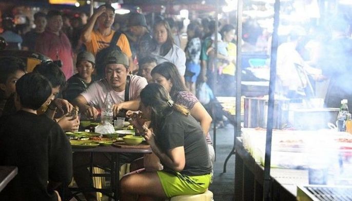 This photo taken on Jan. 30, 2024 shows people enjoying grilled food at an eatery by a roadside market in Manila.