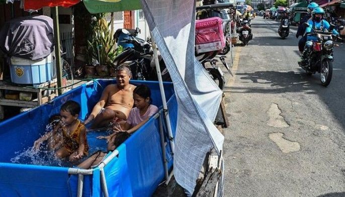 Children and an adult cool off in a makeshift pool beside a street on a hot day in Manila on April 1, 2024.