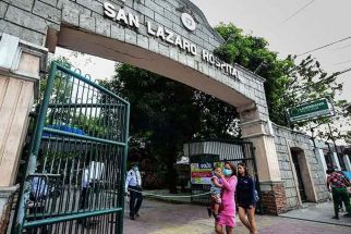 People wearing face masks walk past the main gates of the San Lazaro Hospital in Manila on February 2, 2020.