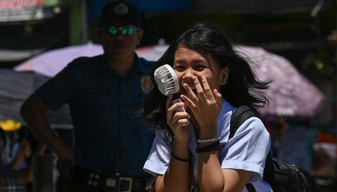 A student uses a portable fan outside a school in Manila on April 2, 2024. More than a hundred schools in the Philippine capital shut their classrooms on April 2, as the tropical heat hit &quot;danger&quot; levels, education officials said. 