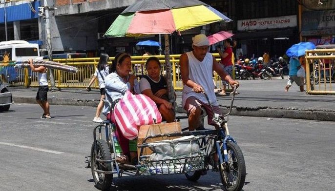 A tricycle rider with a makeshift canopy as protection from the sun transports passengers along a street in Manila on April 25, 2024. Extreme heat is scorching parts of South and Southeast Asia, prompting health warnings from authorities as high temperatures are recorded across the region. 