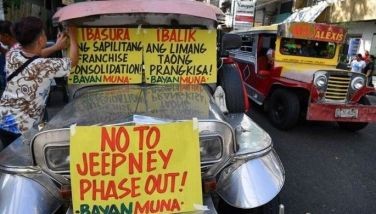 A supporter of drivers of passenger jeepneys displays a banner along a street in Manila on April 29, 2024 on the first day of the jeepney strike ahead of the deadline on April 30 for operators to join a cooperative and gradually replace their fleet with modern vehicles.