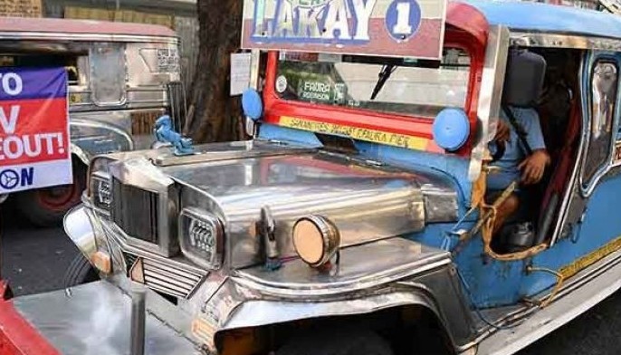 A passenger jeepney speeds past another jeepney displaying a banner along a street in Manila on April 29, 2024 on the first day of the jeepney strike ahead of the deadline on April 30 for operators to join a cooperative and gradually replace their fleet with modern vehicles.