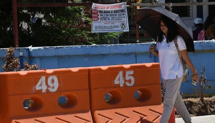 In this photo taken on May 7, 2024, a pedestrian holding an umbrella, as protection from the sun, walks past road barriers with numbers along a highway in Laoag City, north of Manila.