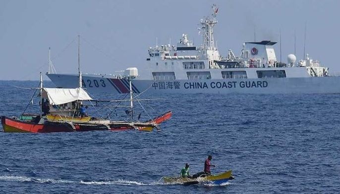 A China Coast Guard ship monitors Philippine fishermen aboard their wooden boats during the distribution of fuel and food to fishers by the civilian-led mission Atin Ito (This Is Ours) Coalition, in the disputed South China Sea on May 16, 2024. 