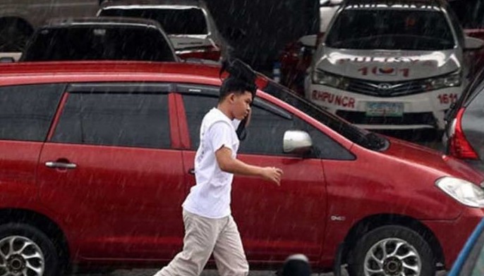 A pedestrian uses his bag to shield himself from the sudden downpour in Quezon City on May 25, 2024.