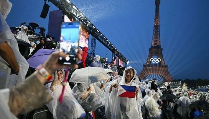 Attendees wearing rain covers pose with a flag of the Philippines in the stands at the Trocadero during the opening ceremony of the Paris 2024 Olympic Games in Paris on July 26, 2024, with the Eiffel Tower in the background.