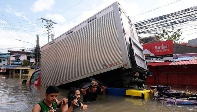 People wade through a flooded road brought about by Tropical Storm Trami, in Naga, Camarines Sur on October 25, 2024. Philippine rescue workers battled floodwaters on October 25 to reach residents still trapped on the roofs of their homes as Tropical Storm Trami moved out to sea after killing at least 40 people. 