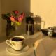 A warm sunlit corner with a coffee cup, open book, and flowers.