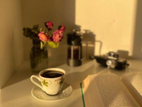 A warm sunlit corner with a coffee cup, open book, and flowers.
