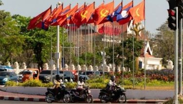 Motorists drive past Laos national flags and Lao People's Revolutionary Party flags ahead of the election in Vientiane on February 19, 2026.