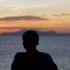 Silhouette of a person leaning on a railing, admiring a serene ocean sunset.