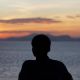 Silhouette of a person leaning on a railing, admiring a serene ocean sunset.